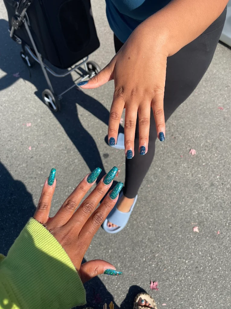 Deep teal and blue nail art on two hands outdoors